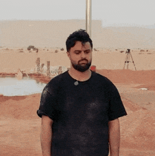 a man with a beard and a black shirt is standing in a desert .