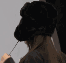 a woman wearing a black fur hat with a flower on it .
