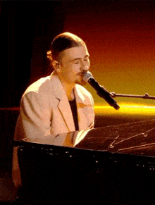 a man in a white suit is singing into a microphone while playing a piano