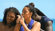 a group of people are standing on a beach and one of them is covering her face with her hand .