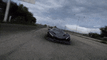 a black car is driving down a road with a cloudy sky in the background