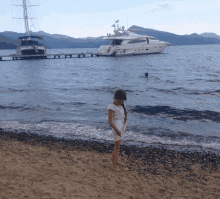 a little girl stands on a beach in front of a large boat