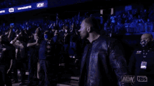 a man in a leather jacket is walking through a crowd of people in a wrestling ring .
