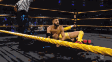 a wrestler is laying on the ground in a wrestling ring with a referee in the background