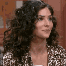 a woman with curly hair is wearing a leopard print shirt and holding a cup .