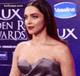 a woman in a strapless dress is standing on a red carpet in front of a vaseline logo .
