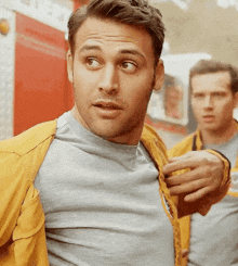 a man in a yellow jacket is standing next to another man in a gray shirt
