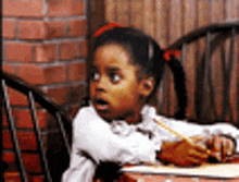 a little girl is sitting at a table with a pencil