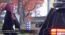 a woman with purple hair is walking towards a car that says abc news on the bottom