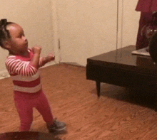 a little girl in a pink and white striped shirt is standing in front of a coffee table
