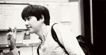 a black and white photo of a young man giving the peace sign while holding a backpack .