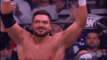 a shirtless wrestler is raising his arms in the air in front of a crowd of people .