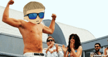 a shirtless man wearing sunglasses is flexing his muscles in front of a group of people