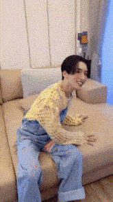 a man is sitting on a couch wearing a yellow sweater and blue overalls .