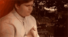 a young man is sitting on a bench holding a rosary in his hands .