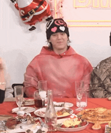 a man in a pink hoodie sits at a table with plates of food and glasses of wine