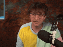 a man wearing glasses and a colorful sweater stands in front of a microphone holding a skeleton
