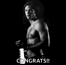 a shirtless man with a tattoo on his chest is standing in the dark and says congrats !