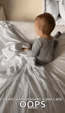 a baby is sitting on a bed with a white blanket and a happy anniversary a day late message .