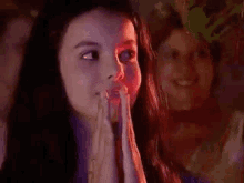 a woman is smiling and clapping her hands in a dark room with a group of people in the background .