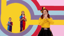 a woman in a yellow sweater is clapping her hands in front of a colorful background .