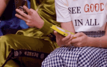 a person wearing a shirt that says see good in all is holding a candy bar