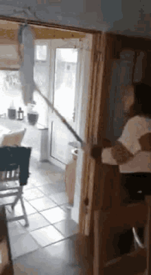 a woman is holding a mop in a kitchen while standing in a doorway .