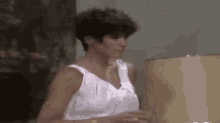 a woman in a white tank top is standing in front of a lamp in a room .
