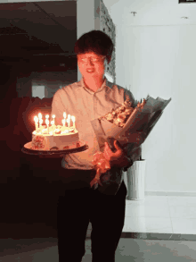 a man holding a bouquet of flowers and a cake with candles on it