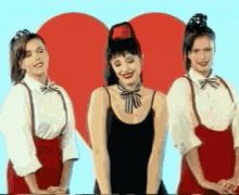 three women are standing in front of a red heart .