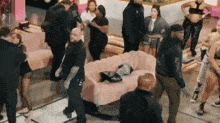 a group of people standing around a pink couch with a man wearing a black shirt that says alpha on it