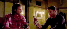 two men are sitting at a table with bottles of beer .