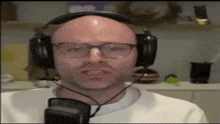 a bald man wearing headphones and glasses is speaking into a microphone .