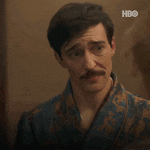 a man with a mustache is wearing a robe and has the word ouch on his chest