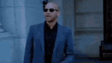 a bald man in a suit and sunglasses is walking down a street .
