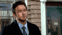 a man in a suit and tie stands in front of a house