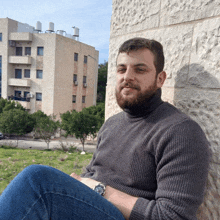 a man with a beard is leaning against a wall with a building in the background