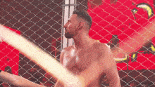 a man without a shirt is standing behind a chain link fence .