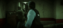 a man in a vest is standing in a dark room with two other men .