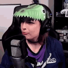 a woman wearing a dinosaur hat is sitting in front of a microphone .
