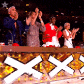 a group of people applauding in front of a sign that has the letter x on it