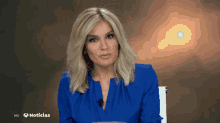a woman in a blue shirt is sitting in front of a hd noticias sign