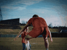 a man in a red shirt is playing soccer with a girl