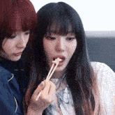 two girls are sitting next to each other and one is eating food with chopsticks