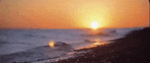 the sun is setting over the ocean and the waves are crashing on the shore .