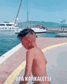 a shirtless boy is standing on a sidewalk next to a body of water with the words opa karkaletsi written on the sidewalk