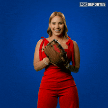a woman in a red dress is holding a baseball glove in front of a blue background that says fox deportes on it