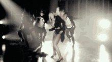 a woman is dancing on a stage with a group of people behind her .