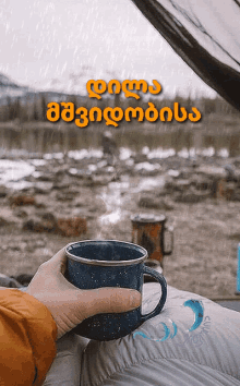 a person is holding a cup of coffee in front of a tent with the words good morning in a foreign language