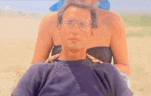 a man wearing glasses is sitting on a beach with a woman in a bikini .